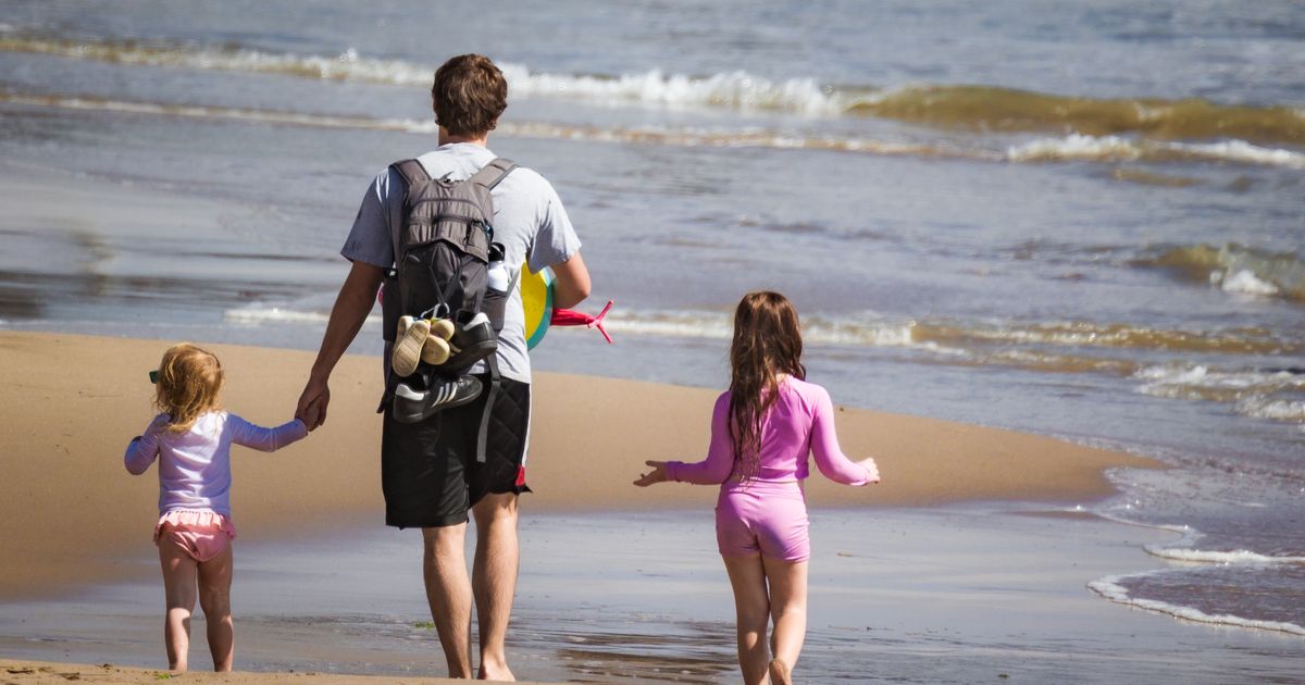 Vader loopt met zijn twee dochters over het strand tijdens de vakantie
