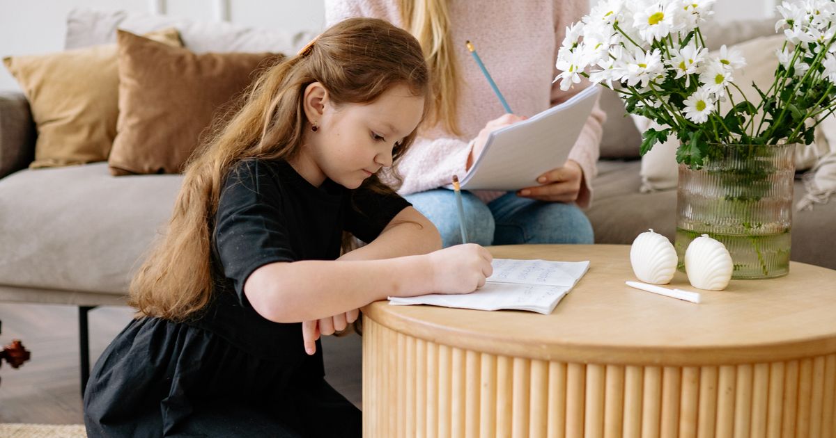 Moeder en dochter maken samen huiswerk aan tafel in de woonkamer
